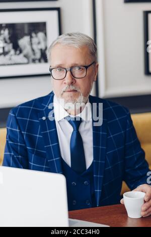 Selbstbewusster Mann sitzt im Büro und trinkt Kaffee. Close up photo.mature Führer der Firma sitzt vor dem Computer und einen Plan Stockfoto
