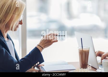 Talentierte erfolgreiche kaukasische Geschäftsfrau erklärt Projektidee im Coffee Shop. Ehrfürchtige Frau zeigt irgendwo während der Arbeit mit einem Mitarbeiter Stockfoto