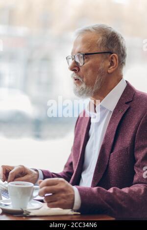 Serious bärtige Mann in roten eleganten Anzug sitzt am Tisch und Surfen im Netz. Alter Mann auf der Suche nach dem Internet conncetion, kostenlose wi-Fi.close up sid Stockfoto