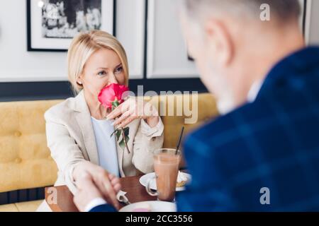 Loving schöne Frau mit Rose auf den Lippen in stilvollen Anzug dankt er Mann für eine Blume. Close up Foto. Stockfoto