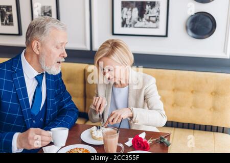 Reifes Paar Verkostung lecker Kuchen. Nahaufnahme Foto. Mann und Frau in stilvollen Anzügen genießen die Dessert Stockfoto