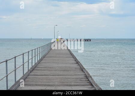 Menschen gehen auf langen hölzernen Kai, die sich über sandige Untiefen weit in tieferes Wasser erstrecken. Stockfoto