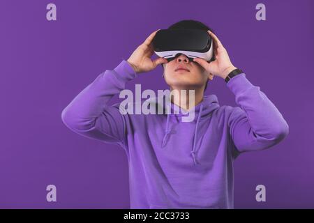 Fröhliche Japanisch in Sport Hoodie, trägt Virtual Reality Helm oder Headset auf dunkelblauem Hintergrund. Smartphone mit Virtual-Reality-Brille. Tec Stockfoto