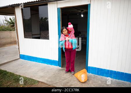 Eine Mutter fastet ihr neugeborenes Baby zu sich zurück in ihrem Zuhause in Manchay Alto, Bezirk Pachamac, Peru. Stockfoto