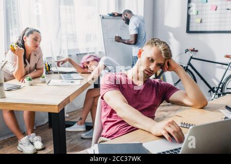 Selektiver Fokus auf junge Geschäftsleute, die auf einem Laptop arbeiten, während sie multikulturell sind Kollegen fühlen sich im Büro heiß Stockfoto