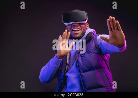 Afrikanischer Profi-Boxer in beiläufiger lila Kleidung schaut sich mit seiner Teilnahme durch den Wettbewerb, mit VR-Brille, studiert Fehler und Takteen Stockfoto