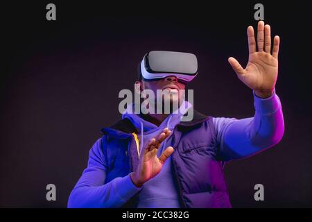 Afrikanischer Profi-Boxer in beiläufiger lila Kleidung schaut sich mit seiner Teilnahme durch den Wettbewerb, mit VR-Brille, studiert Fehler und Takteen Stockfoto