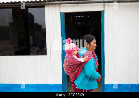 Porträt einer Mutter, die ein Baby auf dem Rücken trägt, in ihrem Zuhause in Manchay Alto, Bezirk Pachamac, Peru. Stockfoto