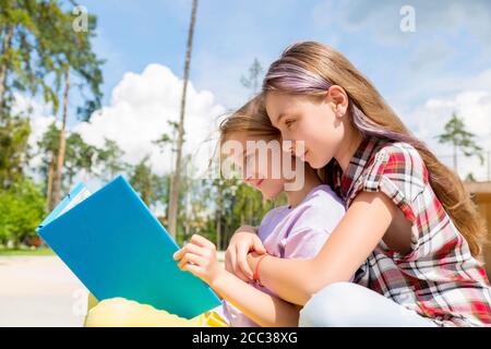 Zwei Schülerinnen sitzen auf einer Bank im Park und machen Hausaufgaben Stockfoto