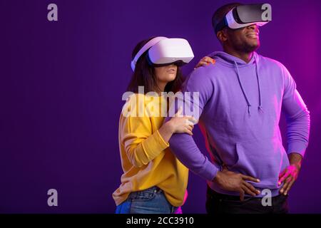 Technologie- und Innovationskonzept. Zwei multikulturelle fröhliche Menschen, in gelben und violetten Farben gekleidet, stehen Seite an Seite mit VR-Brille Ove Stockfoto
