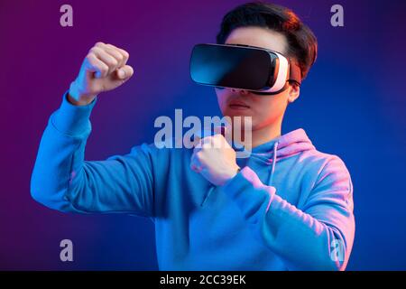 Junge Asiaten bei der Wiedergabe von 3D-Film mit Virtual reality Headset, über dunkle violette Hintergrund posiert isoliert aufgeregt. Stockfoto