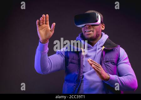 Junge dunkelhäutige Mann in Outdoor-Kleidung mit auf dem Kopf gekleidet Mobile Virtual Reality-Headset für 3D-Spiel aber die Menschheit zu spielen Trifft eine neue Ära der contro Stockfoto