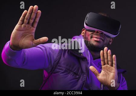 Junge dunkelhäutige Mann in Outdoor-Kleidung mit auf dem Kopf gekleidet Mobile Virtual Reality-Headset für 3D-Spiel aber die Menschheit zu spielen Trifft eine neue Ära der contro Stockfoto
