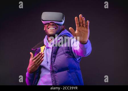 Junge dunkelhäutige Mann in Outdoor-Kleidung mit auf dem Kopf gekleidet Mobile Virtual Reality-Headset für 3D-Spiel aber die Menschheit zu spielen Trifft eine neue Ära der contro Stockfoto