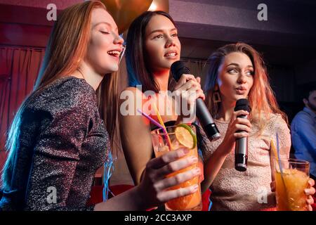 Gut aussehende Damen und Herren haben Freizeit in Karaoke-Bar, tanzen, Spaß zusammen im Karaoke-Club, trinken und essen Stockfoto
