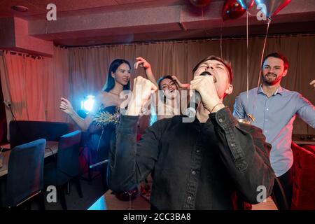 Emotionaler kaukasischer Sänger männlich chave Spaß in Karaoke-Bar, singen im Mikrofon, rocken und chillen im Sängerclub. Stockfoto