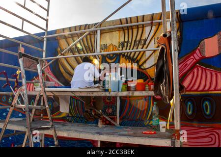 Berlin, Deutschland 09/14/2009: Ein älterer Mann sitzt auf einem Arbeitsgerüst voll von Malausrüstungen und malt ein Bild auf Berliner Mauer mit hallo Stockfoto