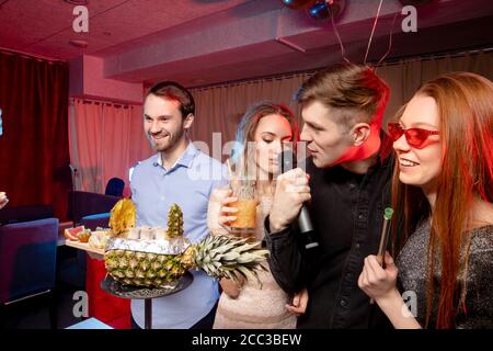 Fröhliche junge kaukasische Menschen haben positive Stimmung, während sie Zeit in Karaoke-Bar verbringen, attraktive Damen und gutaussehende Jungs feiern, haben Party ind Stockfoto