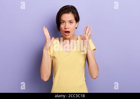 Überrascht junge emotionale Frau mit kurzen schwarzen Haaren schreien, expressing Schock, hält Palmen in der Nähe Gesicht über violetten Hintergrund.isoliert blau backgrou Stockfoto