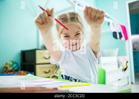 Liebenswert Kleinkind Mädchen Zeichnung mit Bleistiften zu Hause sitzen am Tisch. Kreatives Kind sitzt in einem Raum zu lernen, zu zeichnen. Kleinkind Mädchen tun Stockfoto