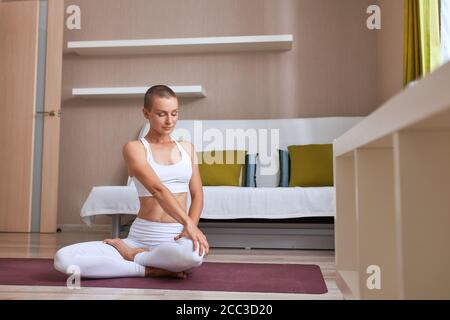 Attraktive kaukasische Mädchen Üben zu Hause in helles Zimmer, Beine überkreuzt. Weiß speziellen Anzug, Thema und Leggins Stockfoto