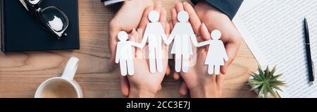 Panoramischer Ernte von Rechtsanwalt und Frau halten Papier geschnitten Familie in der Nähe Tasse, Versicherungsvertrag, Notebook und Pflanze Stockfoto