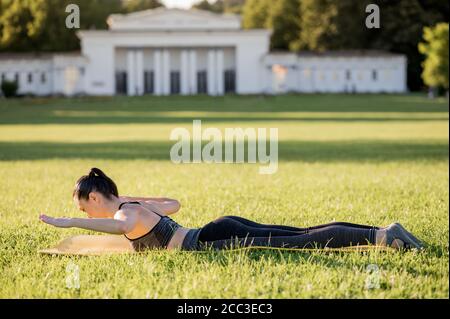 Schöne junge Frau auf einer gelben Matratze liegen, Pose, während das Tragen eines engen Sport-Outfit im Park tun Pilates oder Yoga, der Schwan Tauchanfänger e Stockfoto