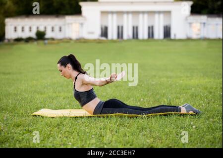Schöne junge Frau liegt auf einer gelben Matratze, Pose, während das Tragen eines engen Sport-Outfit im Park Pilates oder Yoga, Schwan Tauchen Experte exercis Stockfoto