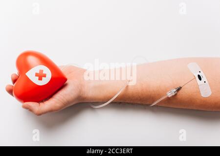 Abgeschnittene Ansicht der männlichen Hand mit rotem Herz und Katheter auf weißem Blutspendekonzept Stockfoto