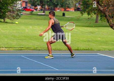 Maryland, USA 08/14/2020: Ein sportlicher hispanic-Mann in einem kurzen und ärmellosen T-Shirt spielt Tennis auf einem lokalen Platz in Baker Park, Frederick. Stockfoto