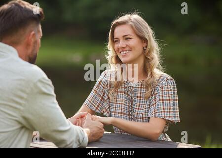 Portrait von schönen Paar Hände halten und Blick auf jeden Andere mit Liebe beim Sitzen am Tisch im Freien am See Bei romantischen Datum Stockfoto