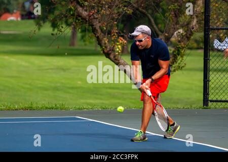 Maryland, USA 08/14/2020: Ein athletischer Kaukasusmann mit blauem T-Shirt und rotem Short spielt Tennis auf einem lokalen Platz in Baker Park, Frederick. H Stockfoto