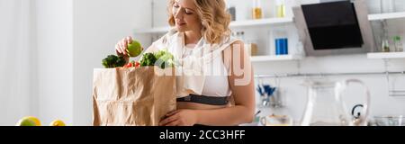 Panorama Ernte der jungen Frau hält Apfel in der Nähe Papiertüte Mit Gemüse Stockfoto