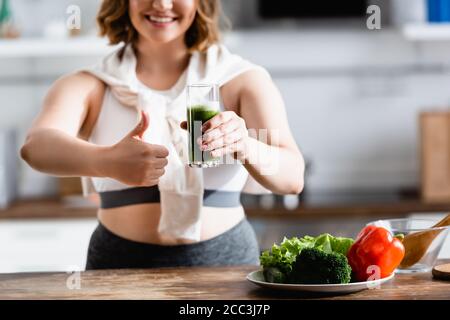 Beschnittene Ansicht der jungen Frau, die Glas grünen Smoothie hält Beim Zeigen des Daumens nach oben Stockfoto