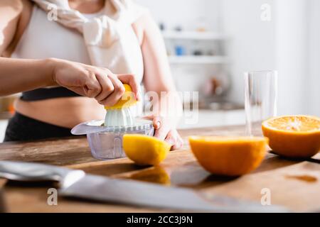 Beschnittene Ansicht einer Frau, die eine Hälfte der Orange in der Nähe des Entsafters hält Beim Zusammendrücken von Früchten Stockfoto