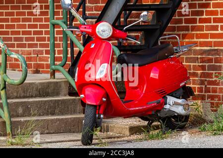 Frederick, MD, 08/14/2020: Ein isoliertes Bild eines roten Vintage Vespa GT200 Motorroller-Motorrades, das vor einem Backsteingebäude durch eine Treppe geparkt wird Stockfoto