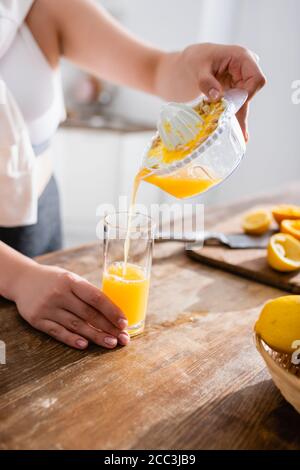 Beschnittene Ansicht einer Frau, die frischen Orangensaft in Glas gießt In der Nähe von gepressten Früchten Stockfoto