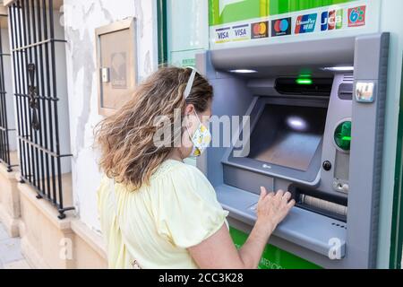 Huelva, Spanien - 16. August 2020: Frau in Schutzmaske benutzt einen Geldautomaten. Neue Normalität in Spanien durch Covid-19 Coronavirus Stockfoto