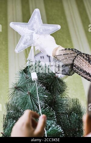 Prozess der Vorbereitung für die Weihnachtsferien. Frau, die den Stern auf den Weihnachtsbaum legt Stockfoto