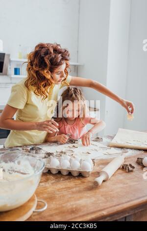 Selektiver Fokus der Mutter Putting Cookie auf Backpapier in der Nähe Tochter Stockfoto