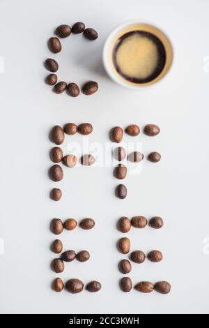 Draufsicht auf Kaffee-Schriftzug aus Bohnen in der Nähe der Tasse Auf weißer Oberfläche Stockfoto