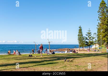 Menschen, die sich im Grass-Bereich vor Dee Why ausruhen Strand an einem sonnigen Herbstnachmittag Stockfoto