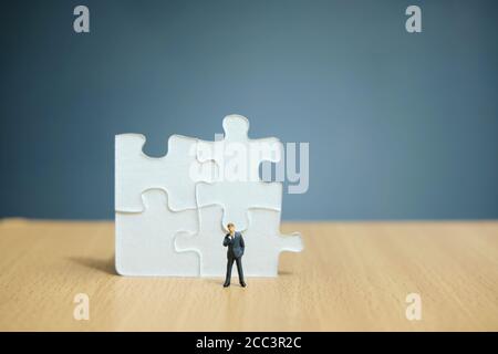 Business-Strategie konzeptuelles Foto - Miniatur Geschäftsmann auf Holz stehen Tabelle vor 4 Stück Puzzle Stockfoto