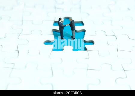 Business-Strategie konzeptionelle Foto - zwei Miniatur Geschäftsmann machen Handschlag Partnerschaftsvereinbarung im fehlenden Puzzleteil Stockfoto