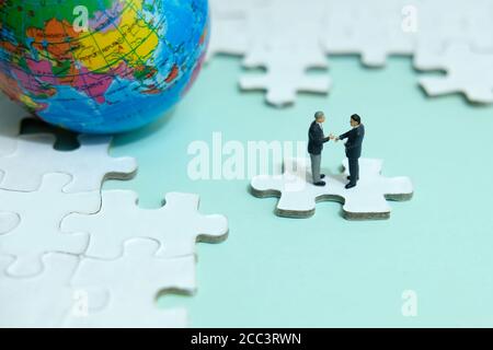 Business-Strategie konzeptionelle Foto - Miniatur Geschäftsmann machen Handschlag Partnerschaft Über Puzzle-Stück mit Globus Stockfoto