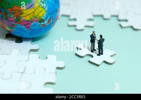 Business-Strategie konzeptionelle Foto - Miniatur Geschäftsmann machen Handschlag Partnerschaft Über Puzzle-Stück mit Globus Stockfoto