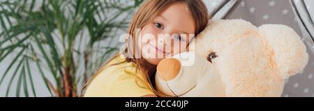 Horizontales Bild des Mädchens, das die Kamera anschaut, während es Teddy umarmt Bär Stockfoto