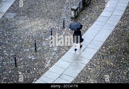 18. August 2020, Berlin: Eine junge Frau geht im Regen mit einem Regenschirm auf einer Straße entlang. Foto: Britta Pedersen/dpa-Zentralbild/dpa Stockfoto