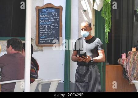 Lissabon, Portugal. August 2020. Ein Kellner mit Gesichtsmaske, Maske wartet auf Gäste vor dem Restaurant, Gastronomie. In Portugal leidet die Tourismusbranche massiv unter den Folgen der Coronavirus-Pandemie - trotz Hochsaison und Urlaubszeit sind die Straßen der Altstadt fast menschenleer, leer. Eindrücke aus Lissabon während der Coronavirus-Pandemie am 16. August 2020. Quelle: dpa/Alamy Live News Stockfoto