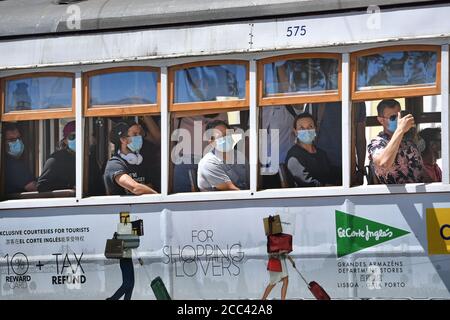 Lissabon, Portugal. August 2020. Passagiere sitzen mit Gesichtsmasken, Masken in einer Straßenbahn, Straßenbahn, Carris, Electrico und schauen aus den offenen Fenstern. In Portugal leidet die Tourismusbranche massiv unter den Folgen der Coronavirus-Pandemie - trotz Hochsaison und Urlaubszeit sind die Straßen der Altstadt fast menschenleer, leer. Eindrücke aus Lissabon während der Coronavirus-Pandemie am 16. August 2020. Quelle: dpa/Alamy Live News Stockfoto